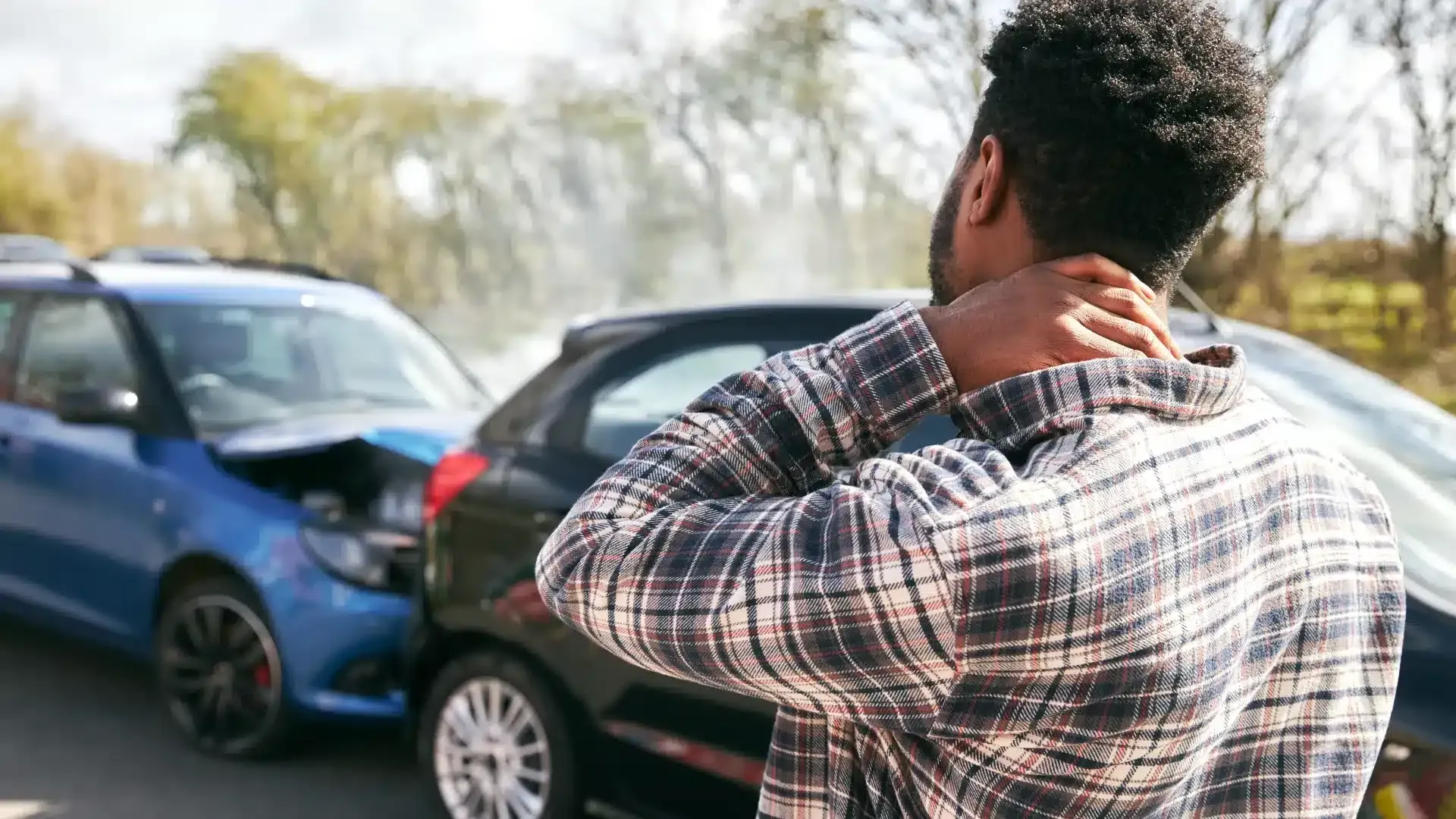 Person looking at a car crash, feeling their neck as it appears to be injured