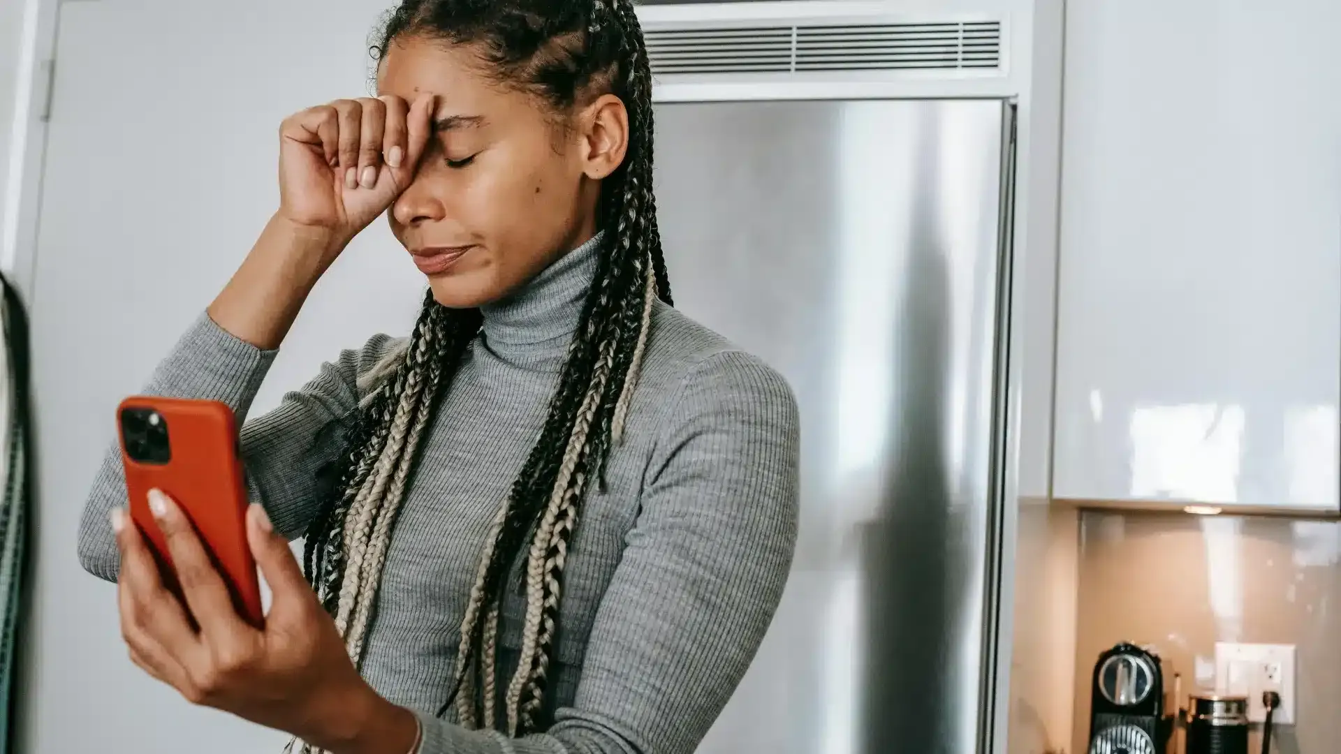 Person holding a phone, with a fist against their head, in distress