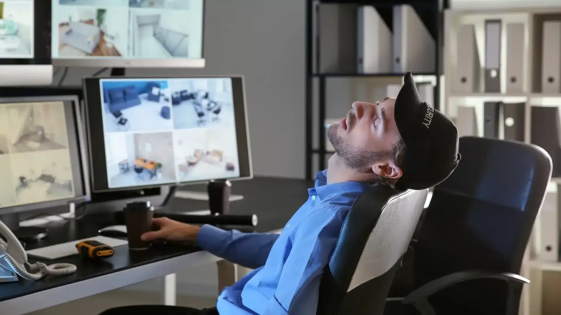 Security guard sit in front of monitors, appears to be sleeping at their position